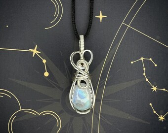 May include: A silver wire-wrapped pendant featuring a moonstone gemstone. The pendant is hanging from a black cord.