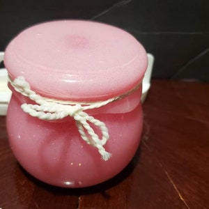 May include: A pink jar with a white string tied around the lid. The jar is filled with a pink glittery substance.
