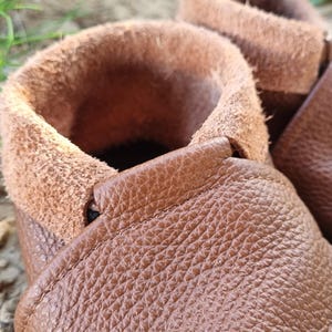 May include: Close-up of a pair of brown leather moccasins with a soft, fuzzy lining. The moccasins have a simple design and are made of high-quality leather.