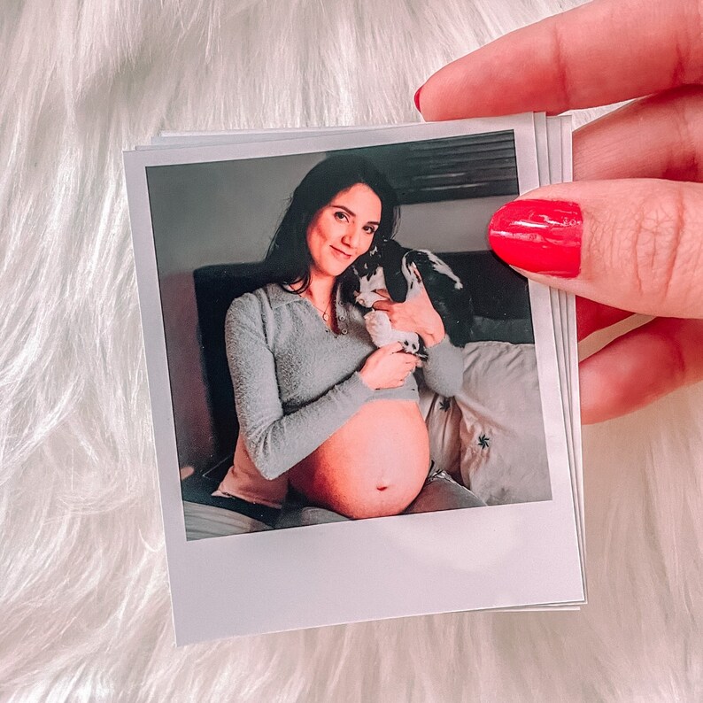 May include: A pregnant woman in a light blue sweater holds a black and white rabbit in her arms. She is sitting on a couch with a white throw blanket.