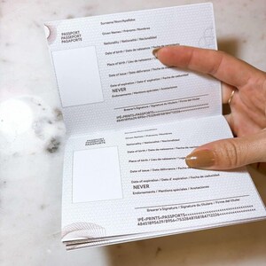 Op de afbeelding: Open paspoort met tekst in het Engels, Frans en Spaans. Het paspoort is open op een pagina met persoonlijke gegevens, waaronder "Geboortedatum", "Geboorteplaats" en "Vervaldatum". De vervaldatum is "NEVER".