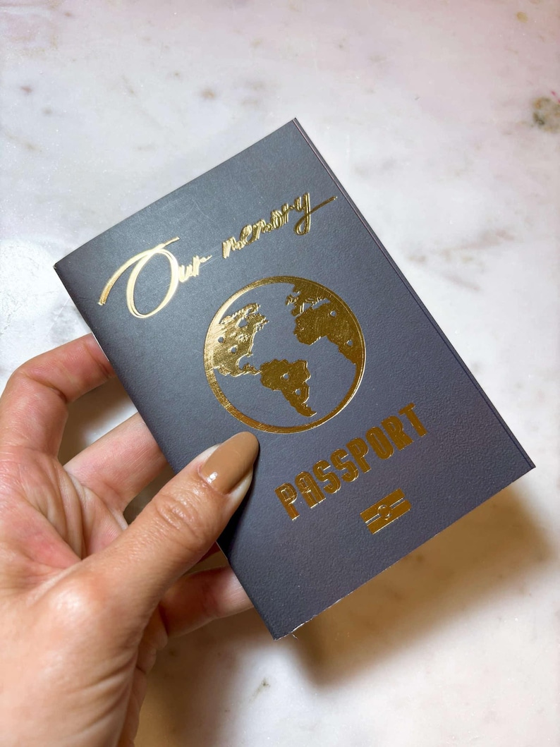 Op de afbeelding: Een donkergrijze paspoort met gouden letters en een wereldkaartontwerp. De tekst "Our memory" staat bovenaan en "PASSPORT" is onder de kaart gedrukt. Onderaan staat een klein gouden embleem.