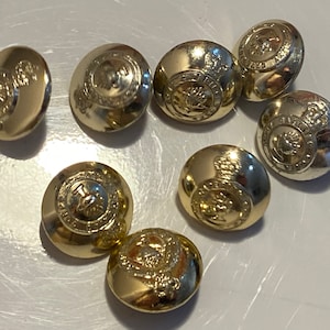 Może przedstawiać: Osiem złotych guzików z wypukłym wzorem. Guziki mają koronę i inne detale.