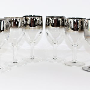 May include: Set of six silver-rimmed wine glasses with a gradient effect. The glasses are clear and have a classic shape.