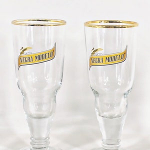 May include: Two clear glass beer glasses with a gold rim and the words "Negra Modelo" printed on the side.