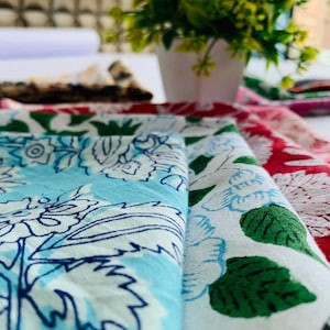May include: A stack of fabric squares with floral patterns in shades of blue, white, and pink. The fabric is folded and layered, showcasing the intricate designs.