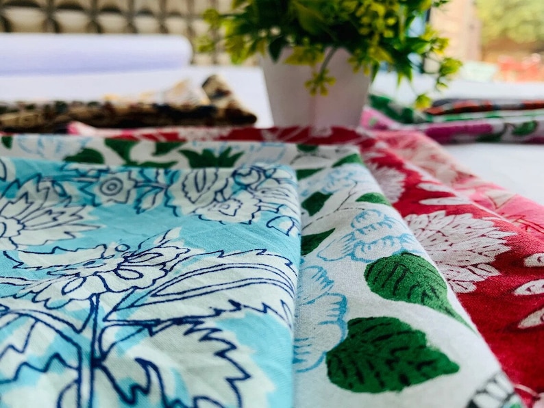 May include: A stack of fabric squares with floral patterns in shades of blue, white, and pink. The fabric is folded and layered, showcasing the intricate designs.