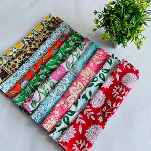 May include: A stack of ten colorful cotton napkins with floral patterns. The napkins are folded and arranged in a fan shape. The napkins are in various shades of red, pink, blue, green, and orange.