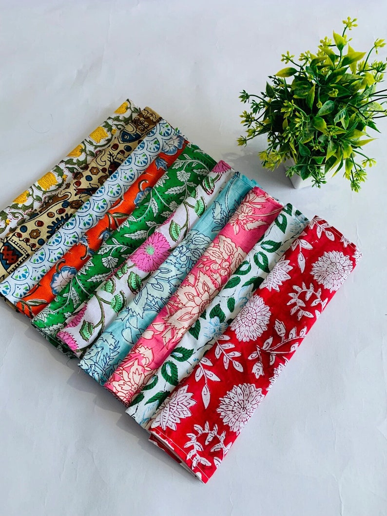 May include: A stack of ten colorful cotton napkins with floral patterns. The napkins are folded and arranged in a fan shape. The napkins are in various shades of red, pink, blue, green, and orange.