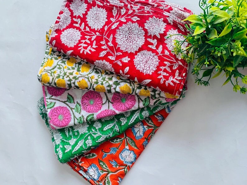 May include: A stack of five colorful cotton napkins with floral patterns. The napkins are in shades of red, yellow, pink, green, and orange.