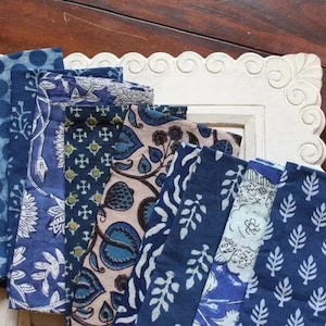 Puede incluir: Un juego de servilletas de tela azul y blanco con patrones. Las servilletas presentan varios dise&ntilde;os, incluyendo patrones florales, geom&eacute;tricos y de hojas. Las servilletas est&aacute;n dispuestas en una pila, con la servilleta superior doblada por la mitad.