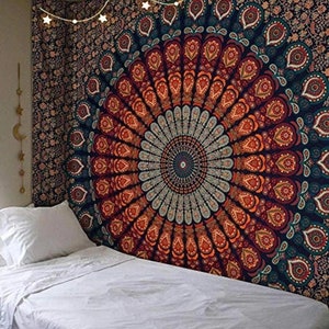 May include: A large, colorful tapestry with a mandala design dominates the image. The tapestry features a circular pattern in shades of orange, red, teal, and blue. The tapestry is hanging above a bed with white linens. String lights with star-shaped bulbs are strung across the top.