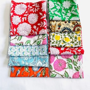 May include: A stack of 10 colorful cotton fabric squares with floral and geometric patterns. The squares are folded and arranged in two rows of five. The fabric is a mix of red, green, blue, yellow, orange, and pink.