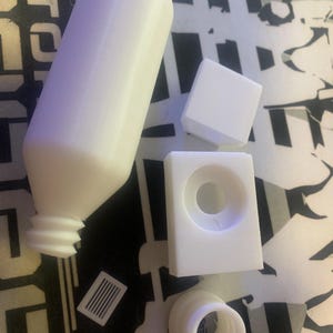May include: A set of white plastic bottle stoppers. The set includes a bottle stopper with a threaded top, a bottle stopper with a round top, and a bottle stopper with a square top.