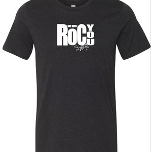 May include: A dark gray t-shirt with a white graphic that says "We Will Rock You" with a chemical structure underneath.