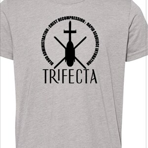May include: A gray t-shirt with a black graphic of a helicopter with a cross on top. The graphic is surrounded by a circle with the text "BLOOD ADMINISTRATION: CHEST DECOMPRESSION: RAPID SEQUENCE INTUBATION" and the word "TRIFECTA" below the graphic.