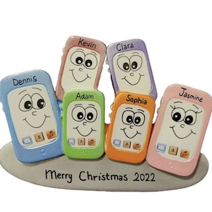 May include: A Christmas ornament featuring six colorful cell phone-shaped figures with smiling faces and names written on them. The ornament reads "Merry Christmas 2022" at the bottom.