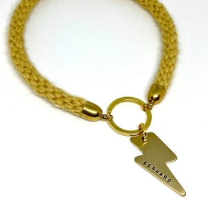 A gold thunder/lightning bolt dog ID Tag with a yellow knitted rope collar with the word 'BERNARD' engraved on it.