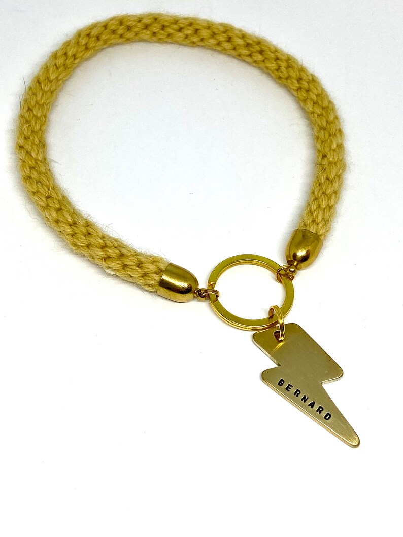 A gold thunder/lightning bolt dog ID Tag with a yellow knitted rope collar with the word 'BERNARD' engraved on it.