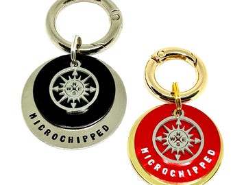 May include: Two pet ID tags with a compass rose design. One tag is black with a silver ring, the other is red with a gold ring. Both tags have the text "MICROCHIPPED" and a silver compass rose.
