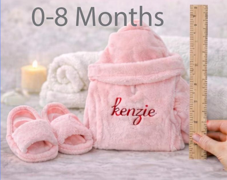 Peut inclure: Ensemble de peignoir et chaussons roses pour b&eacute;b&eacute;. Le peignoir est brod&eacute; du nom "kenzie" en &eacute;criture rouge. L'image comprend &eacute;galement une r&egrave;gle, indiquant la taille des articles. Le texte "0-8 Months" est en haut.