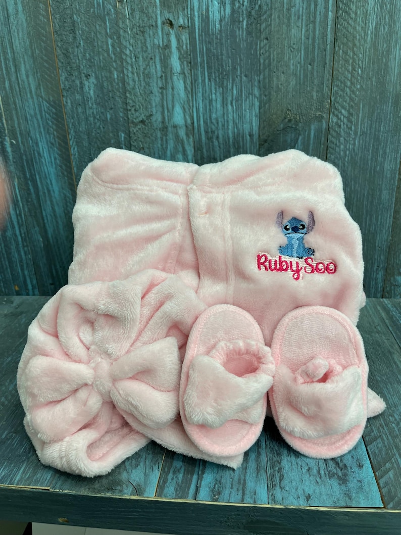 Peut inclure: Ensemble de spa en peluche rose comprenant un peignoir, un bandeau avec un n&oelig;ud et des chaussons. Le peignoir porte une broderie du personnage Stitch et le texte "Ruby Soo". L'ensemble est en mati&egrave;re douce et moelleuse.