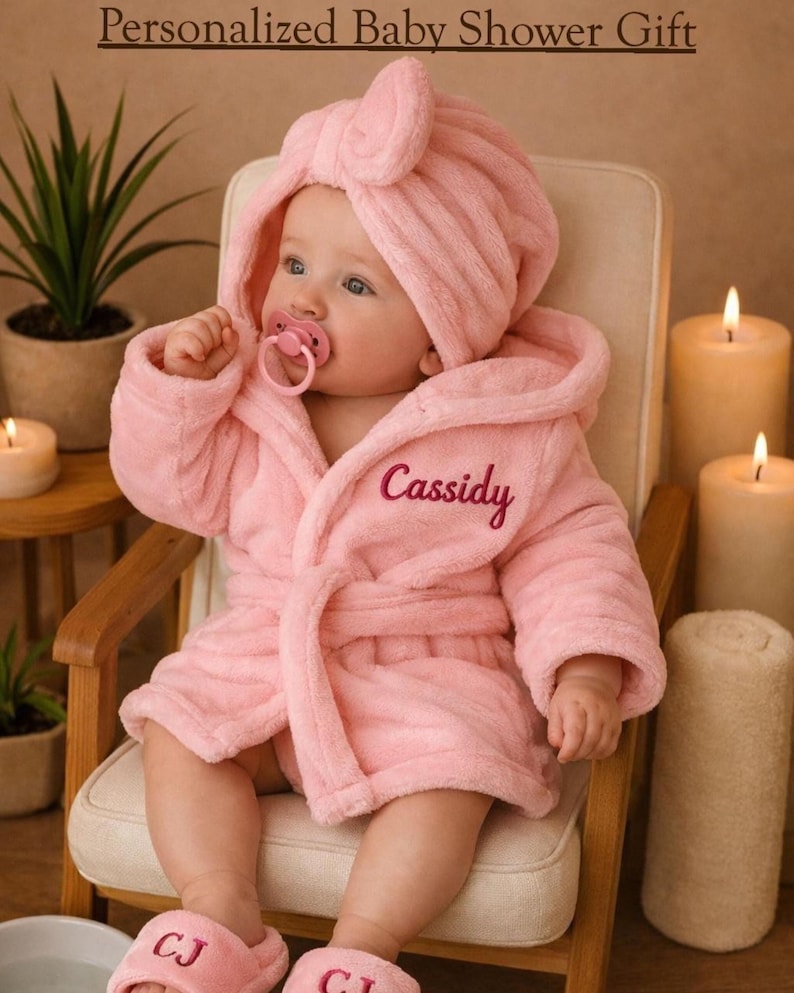 Peut inclure: Un b&eacute;b&eacute; portant un peignoir rose &agrave; capuche, des chaussons assortis et une sucette, assis dans une petite chaise en bois. Le peignoir est brod&eacute; du nom "Cassidy". Le texte "Personalized Baby Shower Gift" est en haut de l'image.