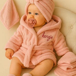 Peut inclure: Un b&eacute;b&eacute; v&ecirc;tu d'un peignoir en &eacute;ponge rose, d'un bonnet turban assorti et de chaussons. Le peignoir est brod&eacute; du nom "kenzie". Une sucette est dans la bouche du b&eacute;b&eacute;. Une d&eacute;barbouillette et une serviette sont &eacute;galement visibles.