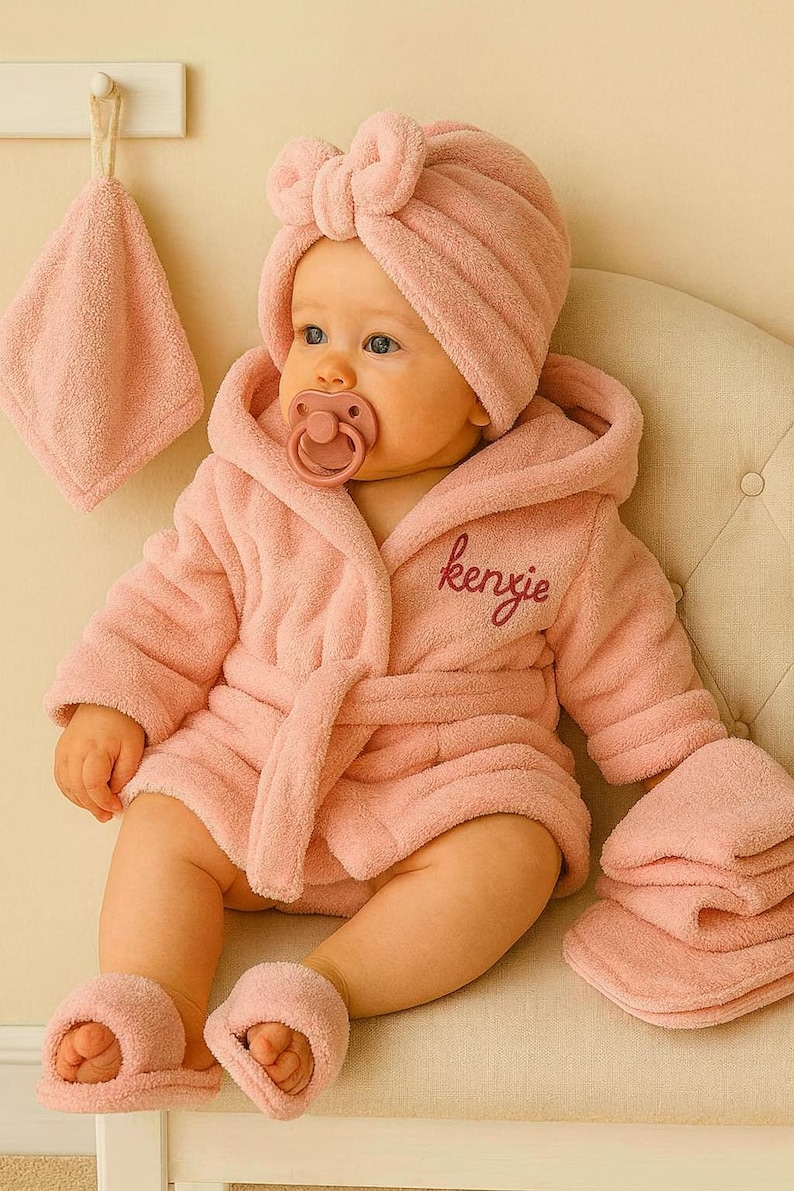Peut inclure: Un b&eacute;b&eacute; v&ecirc;tu d'un peignoir en &eacute;ponge rose, d'un bonnet turban assorti et de chaussons. Le peignoir est brod&eacute; du nom "kenzie". Une sucette est dans la bouche du b&eacute;b&eacute;. Une d&eacute;barbouillette et une serviette sont &eacute;galement visibles.