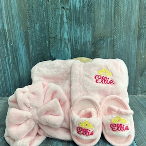 Peut inclure: Ensemble de spa rose en peluche comprenant un bandeau avec un n&oelig;ud, un peignoir et une paire de chaussons. Le peignoir et les chaussons sont brod&eacute;s d'une couronne et du nom "Ellie".