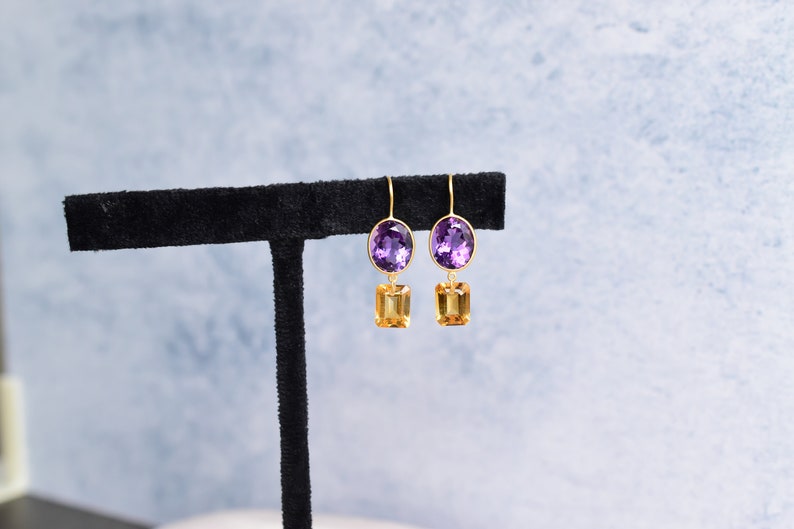 May include: A pair of gold earrings with a purple oval gemstone and a smaller, rectangular, yellow gemstone hanging below.