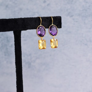May include: Gold earrings with a purple oval-shaped gemstone and a yellow square-shaped gemstone.
