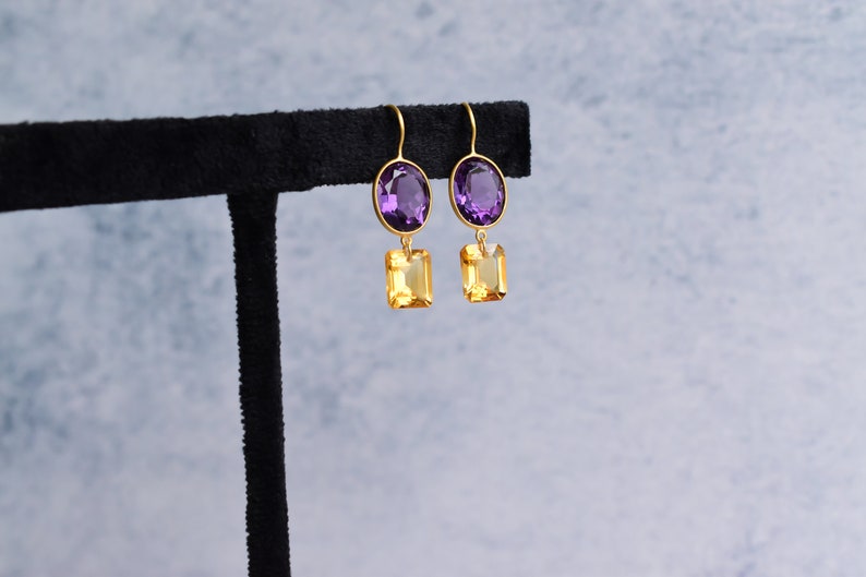 May include: Gold earrings with a purple oval-shaped gemstone and a yellow square-shaped gemstone.