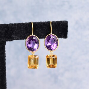May include: A pair of gold earrings with purple oval-shaped gemstones and smaller, square-shaped, yellow gemstones hanging below.