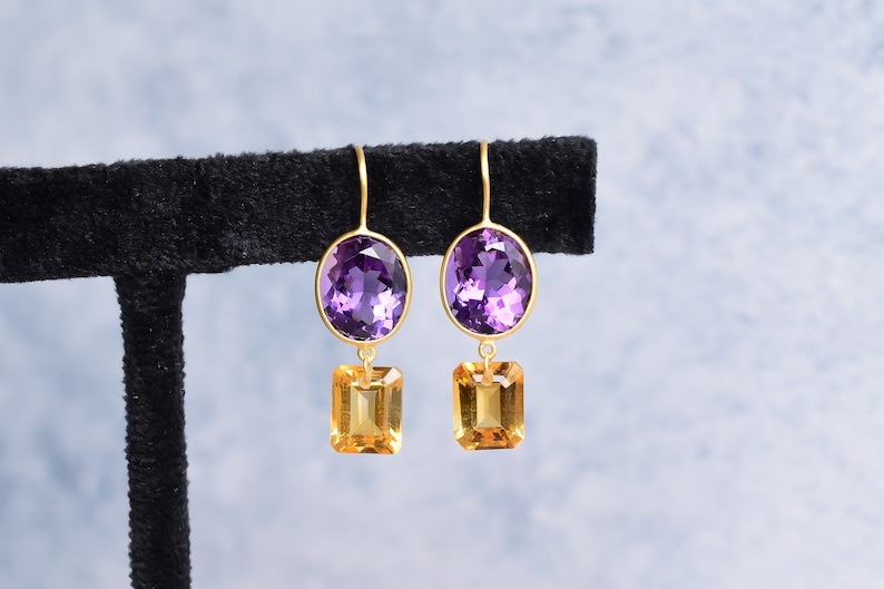 May include: A pair of gold earrings with purple oval-shaped gemstones and smaller, square-shaped, yellow gemstones hanging below.