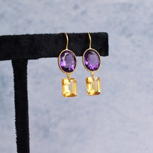 May include: Gold earrings with a purple oval gemstone and a yellow square gemstone.