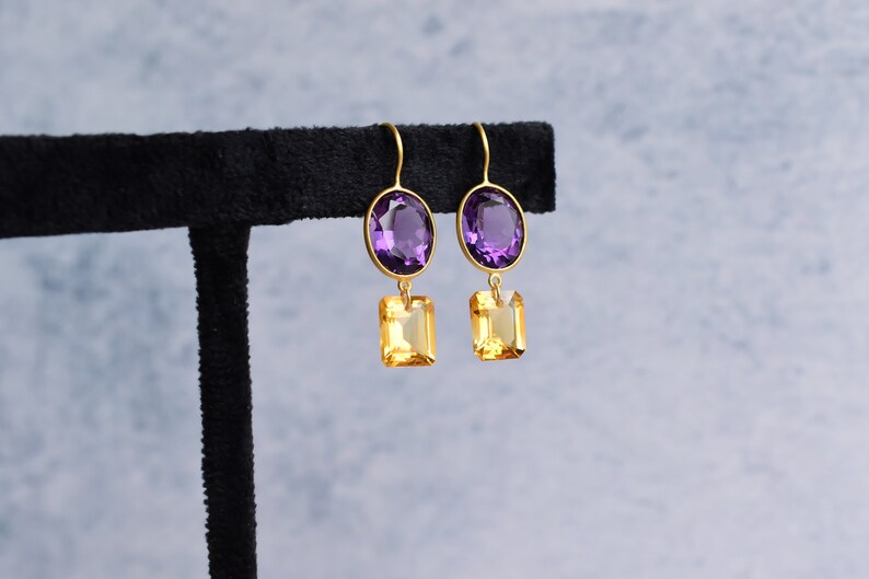 May include: Gold earrings with a purple oval gemstone and a yellow square gemstone.