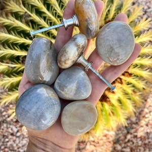 May include: Six natural stone cabinet knobs with silver metal hardware. The knobs are various shades of gray and brown.