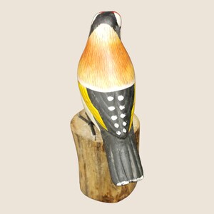 May include: A hand-painted wooden bird figurine with black, yellow, orange, and white details. The bird is perched on a wooden stump.