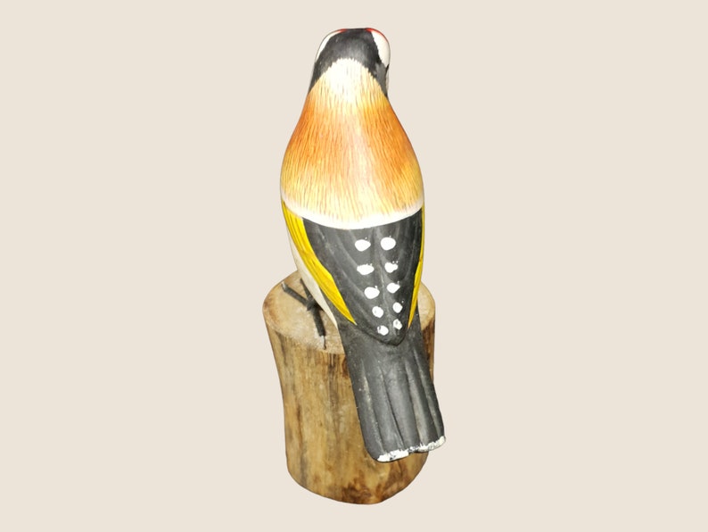 May include: A hand-painted wooden bird figurine with black, yellow, orange, and white details. The bird is perched on a wooden stump.