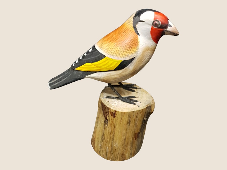 May include: Hand-painted wooden bird figurine of a goldfinch perched on a wooden stump. The bird is painted with realistic details, including black and white markings, a yellow breast, and a red head.