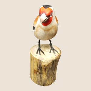 May include: Hand-carved wooden bird figurine with red, black, and white painted details. The bird is perched on a small wooden log.