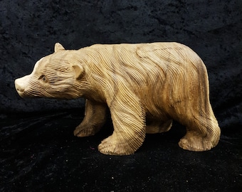 May include: A wooden bear sculpture carved in a walking pose. The bear is light brown and has a detailed fur texture.