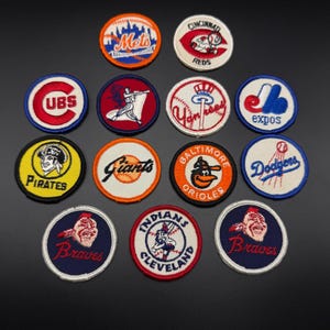 May include: A collection of fourteen circular embroidered baseball team patches featuring various logos and team names including Mets, Reds, Cubs, White Sox, Yankees, Expos, Pirates, Giants, Orioles, Dodgers, and Braves in diverse colors.