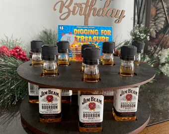 Könnte beinhalten: Ein drehbarer Holzständer mit acht kleinen Flaschen Jim Beam Kentucky Straight Bourbon Whiskey. Der Ständer steht auf einem Holztisch mit einem Schild, auf dem "Happy Birthday" steht, und einem Lottoschein, auf dem "Digging for Treasure" steht.