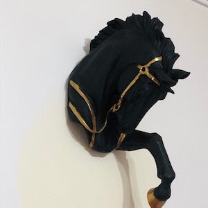 May include: Black horse head wall decor with gold accents. The horse's head is tilted to the side and the horse's mouth is slightly open. The horse's mane is flowing and the horse's tail is curled up.