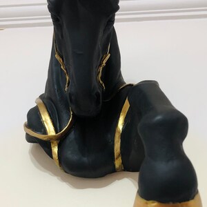 May include: Black horse head sculpture with gold accents. The horse is lying down with its head raised. The sculpture is made of a smooth, black material and has a glossy finish.