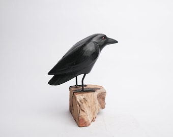 May include: A black wooden crow sculpture with red eyes perched on a natural wood base.