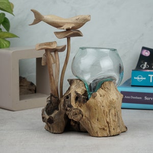 May include: A wooden whale sculpture perched on a mushroom-shaped wooden base, with a clear glass vase nestled in a piece of driftwood. The vase has a teal-colored rim.