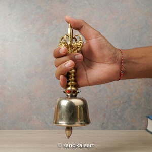 May include: A gold and silver bell with a decorative handle. The bell has a small, pointed tip at the bottom and is adorned with colorful beads.